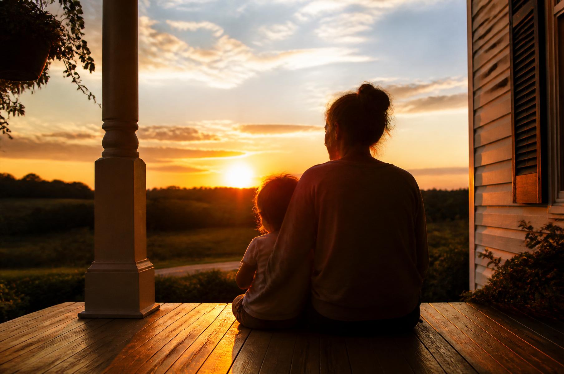 A mother and child watching the sunset from a front porch